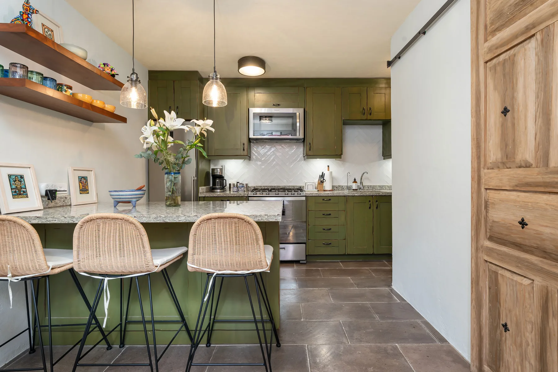 A kitchen with green cabinets, a counter, and seating beneath pendant lights.