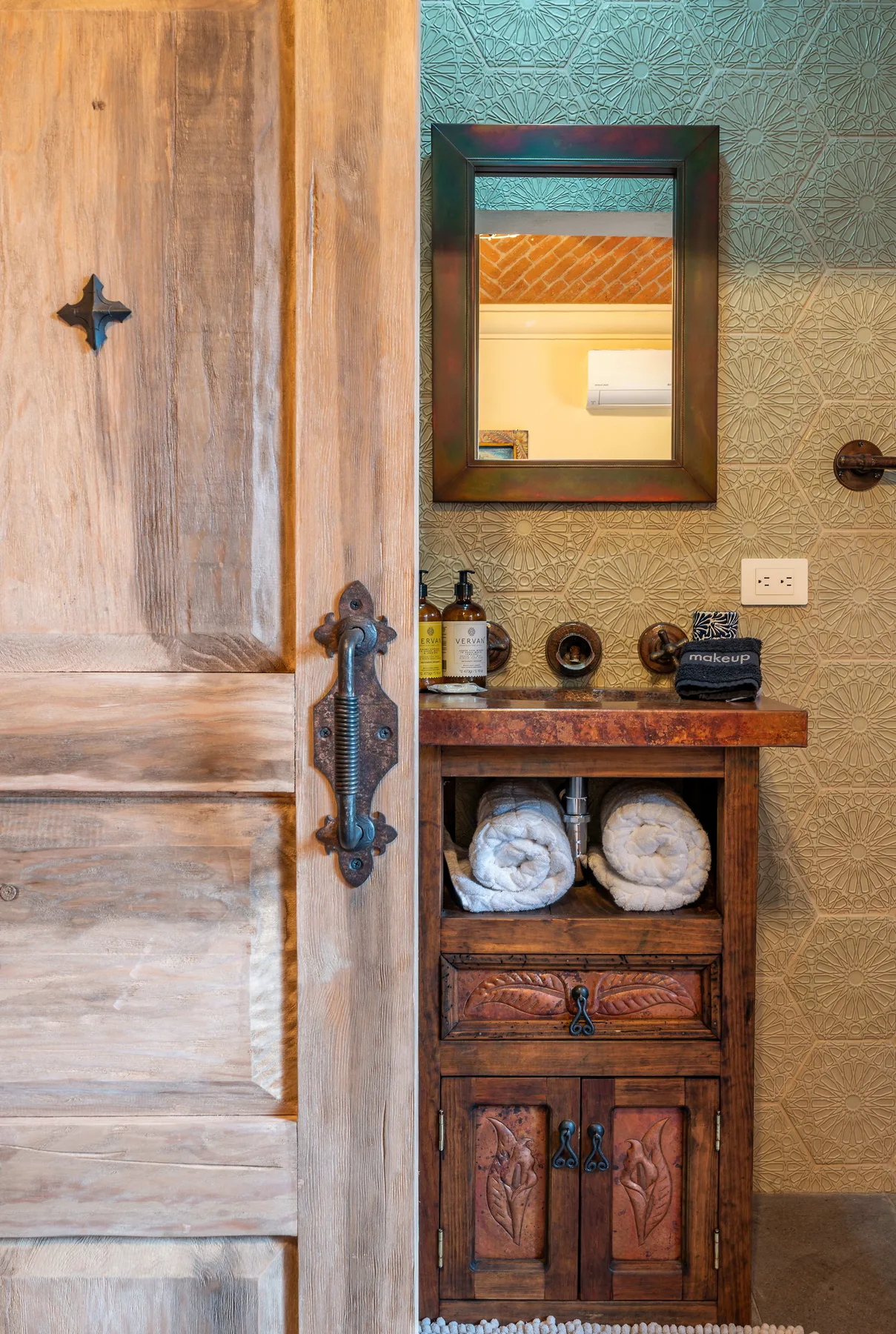 A wooden vanity with folded towels stands beside an open wooden door.