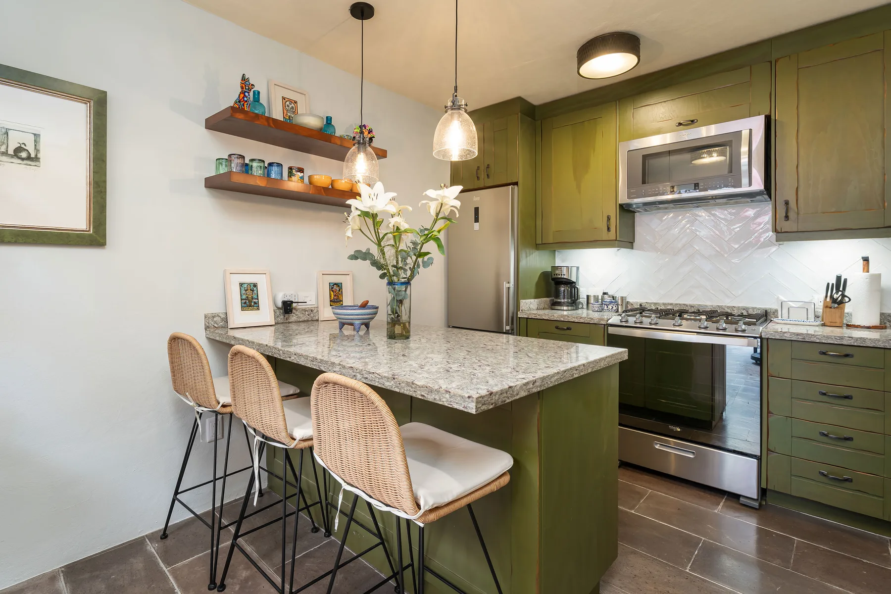 A kitchen with a stone-topped island, bar seating, and green cabinetry.
