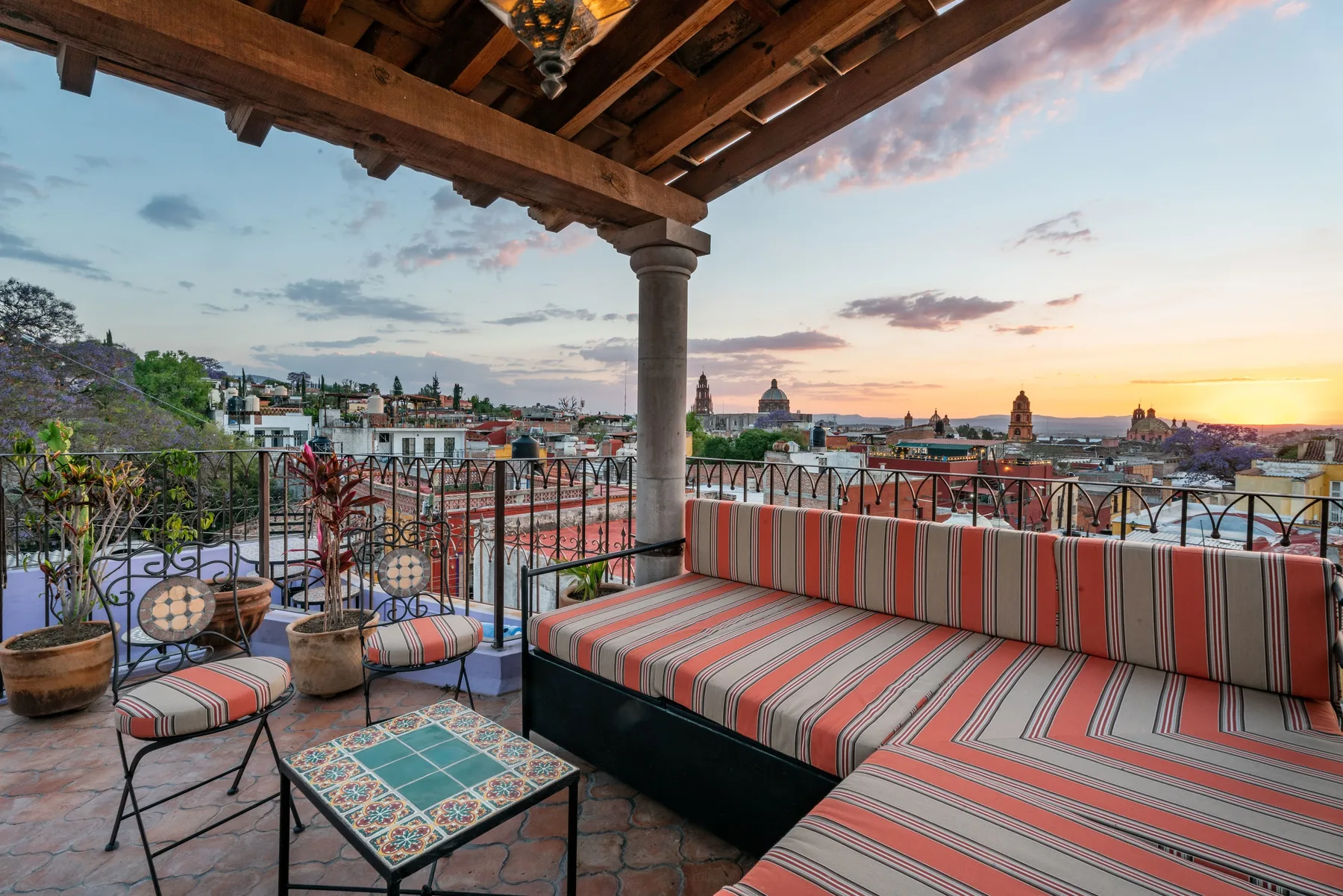 A rooftop terrace with striped seating overlooks the city at sunset.