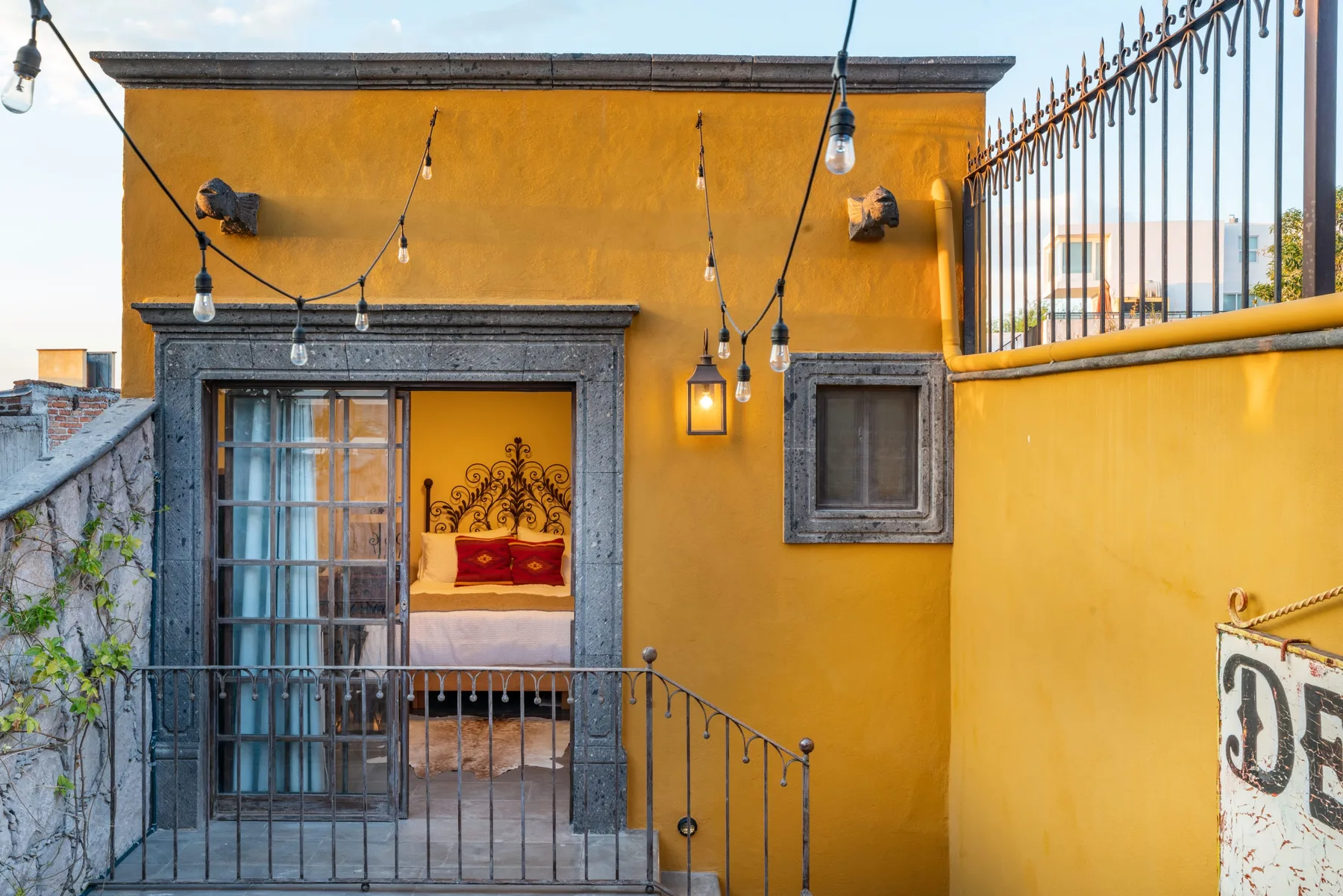 A yellow-walled terrace with a doorway, railing, and string lights.