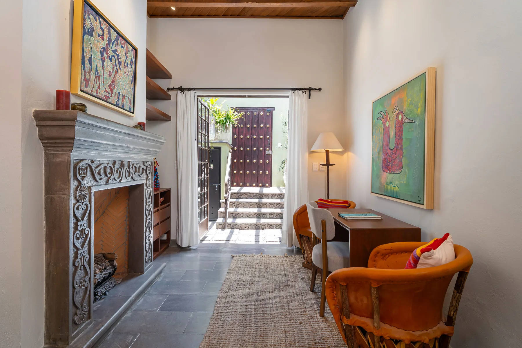 A sitting area with a fireplace, table, and artwork beside an open doorway.