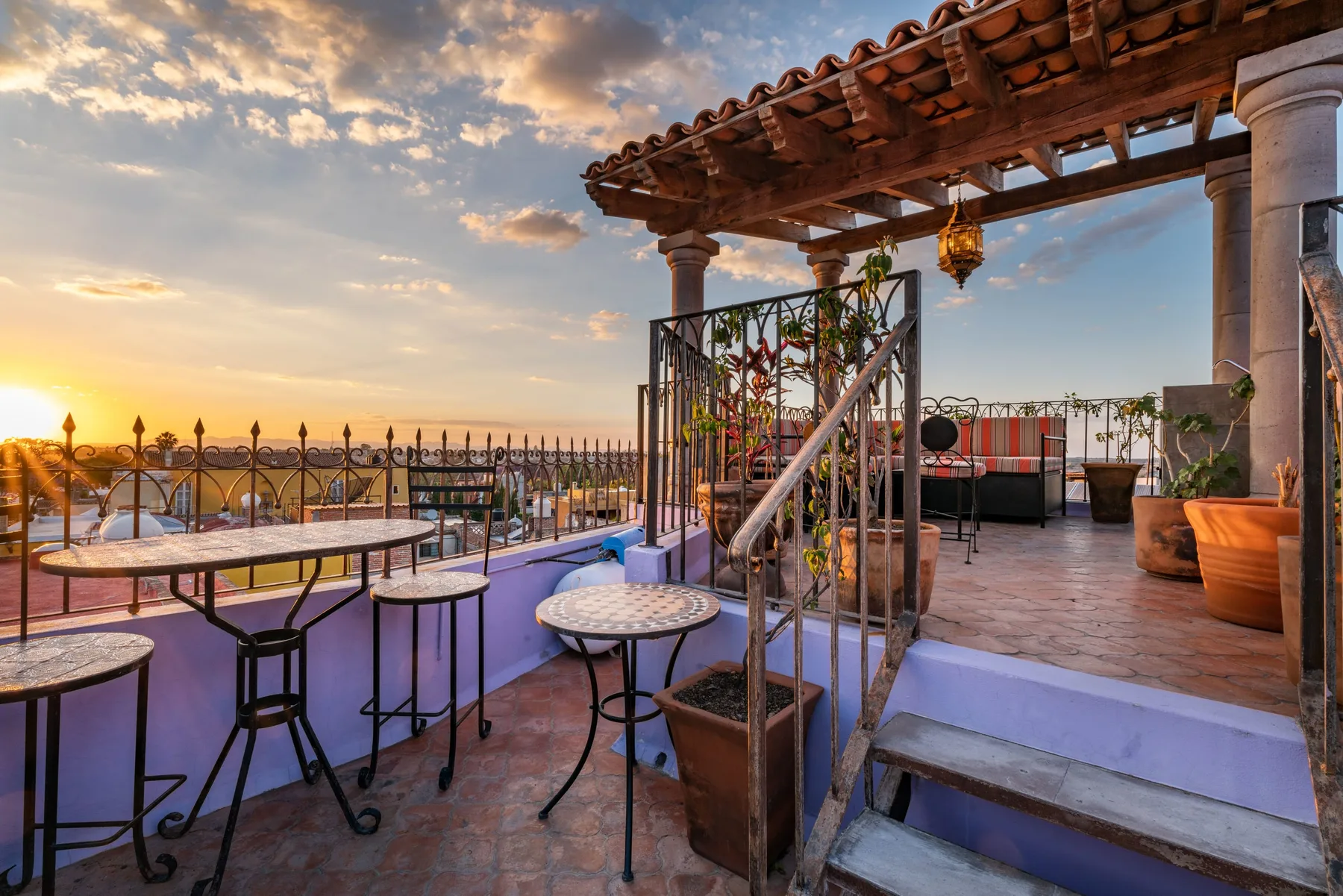 An outdoor terrace with tables and seating beneath a wooden pergola at sunset.