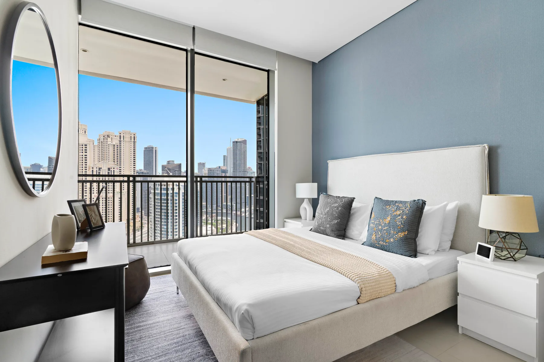 Un dormitorio con una cama bien tendida junto a grandes ventanas con vistas a la ciudad.