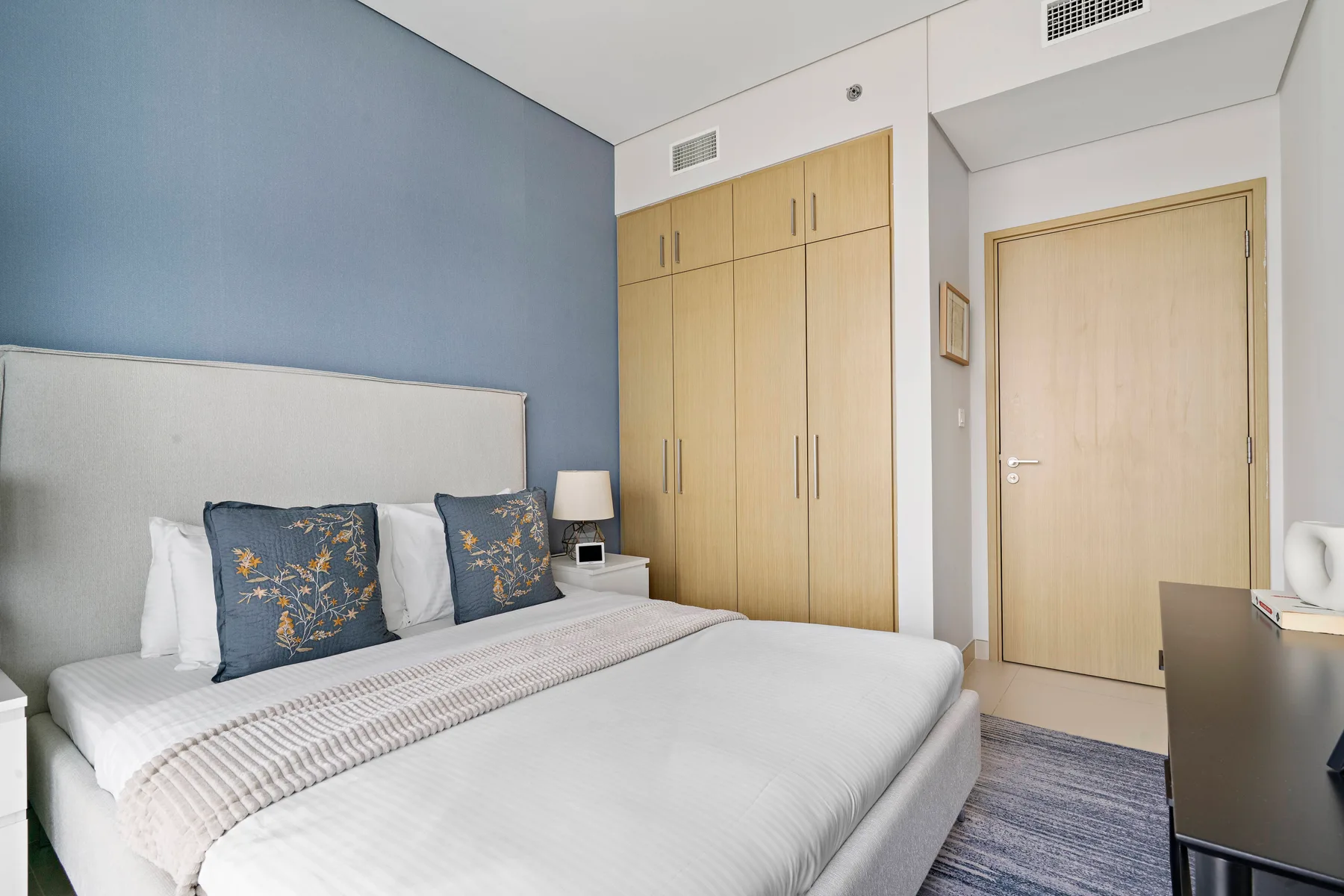 Un dormitorio con una cama bien tendida, armarios de madera clara y una pared azul.