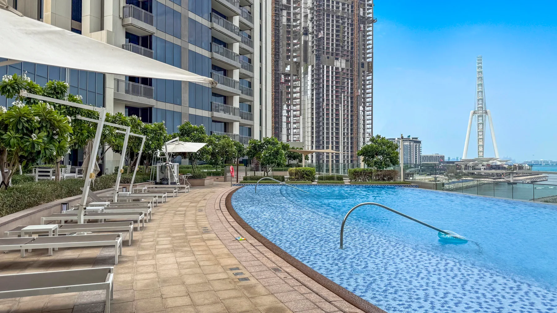 Zona común: Una piscina junto a edificios altos y una terraza pavimentada.