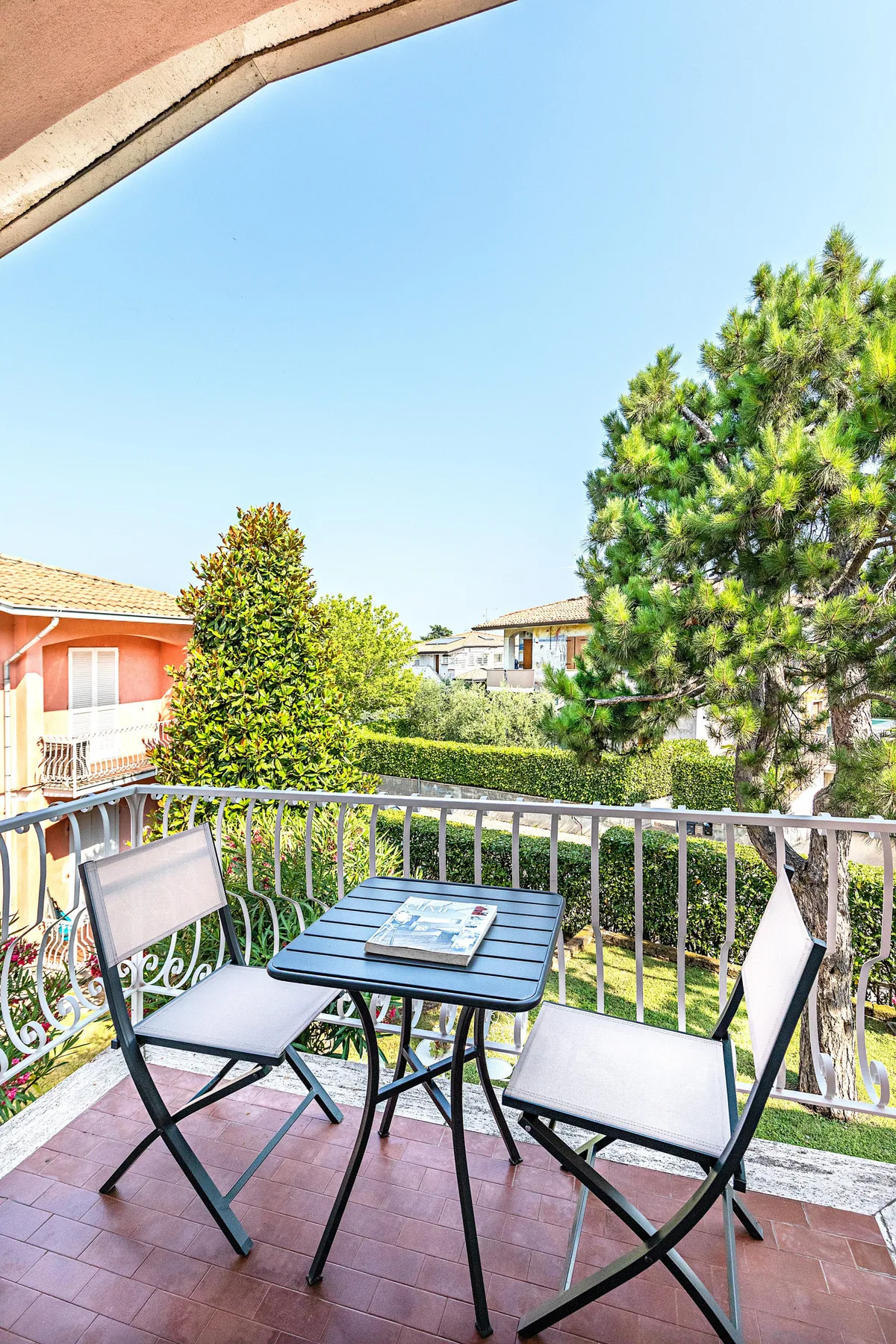 A balcony seating area with a small table overlooks trees and nearby buildings.