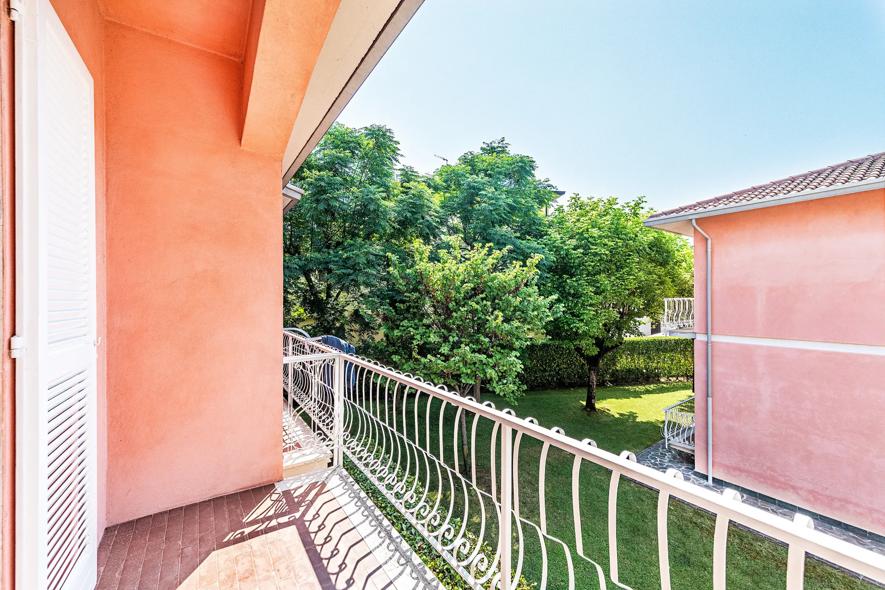 A balcony overlooks a green courtyard with trees and neighboring buildings.