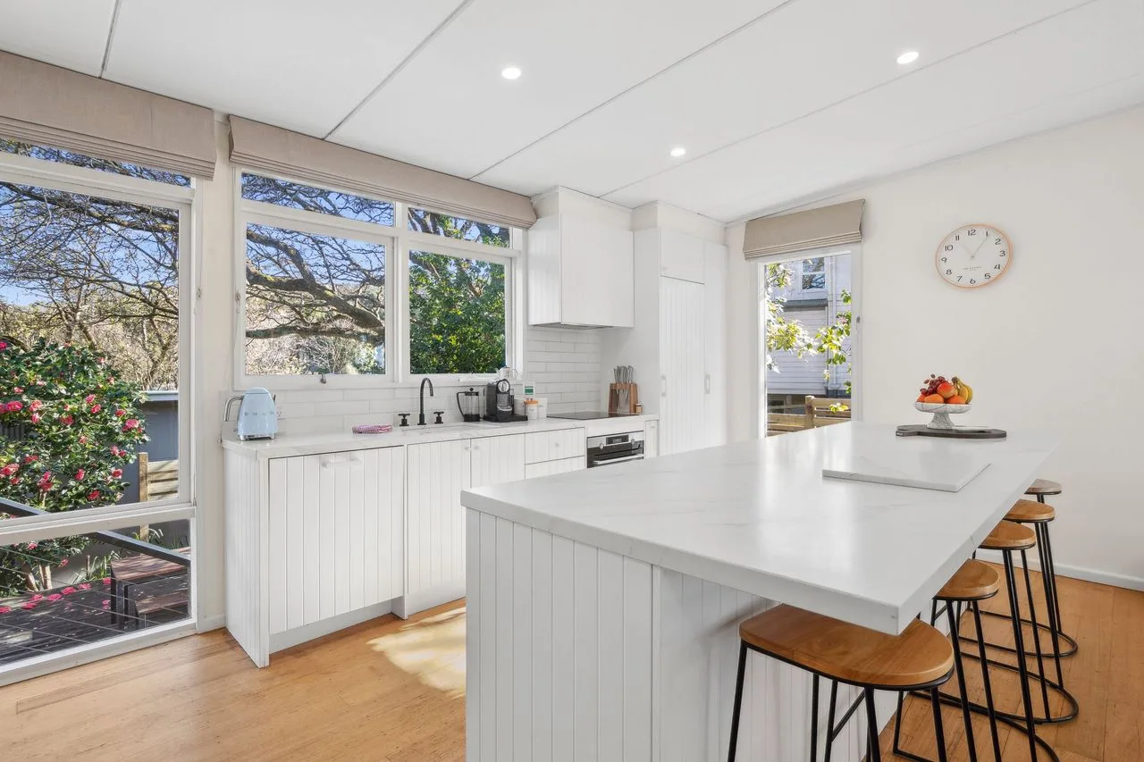 A bright white kitchen with a large island and windows overlooking greenery.