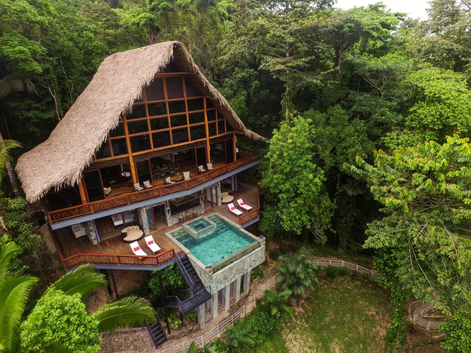 A thatched-roof building with open balconies sits amid dense tropical greenery.
