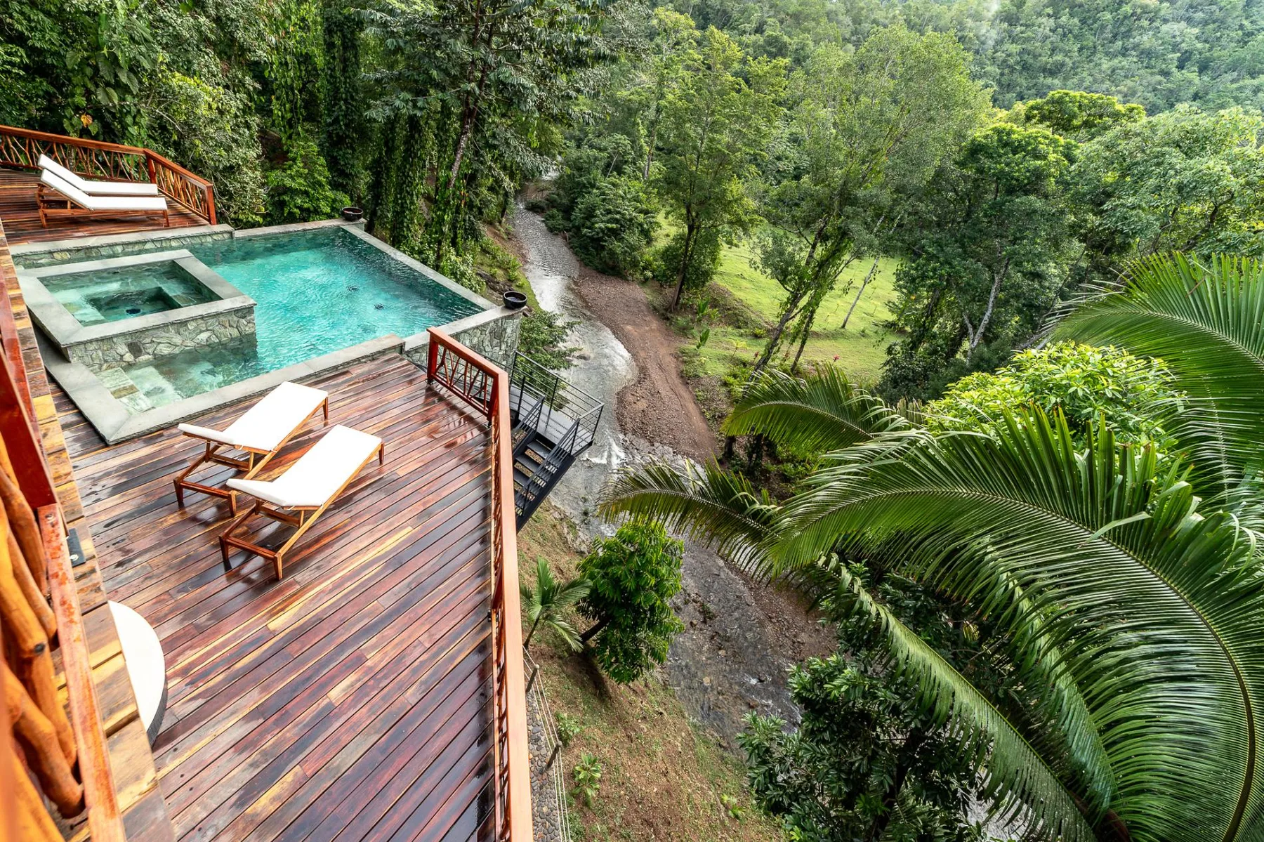 A wooden deck with a pool overlooks a lush, tree-filled landscape.