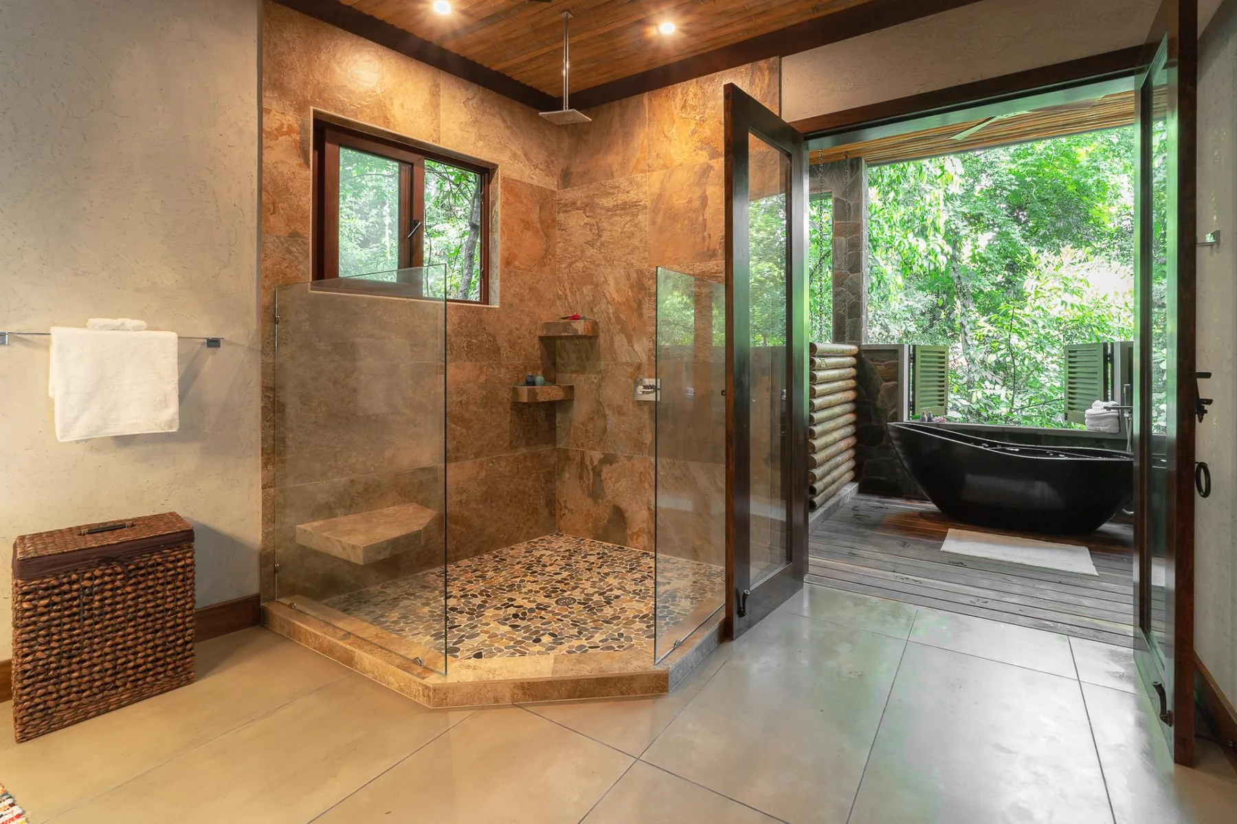 A bathroom with a glass shower and an open doorway overlooking a tub and greenery.