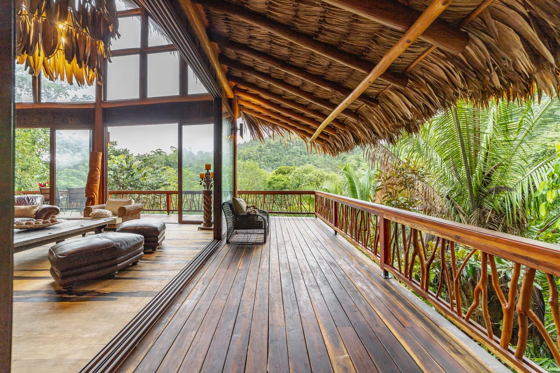 A spacious wooden deck with lounge seating opens onto lush tropical greenery.