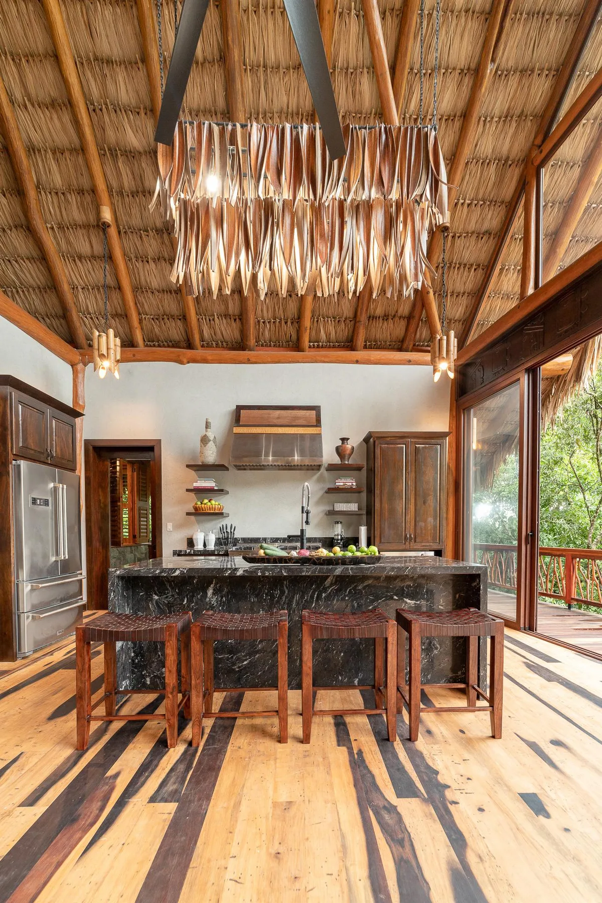 An open kitchen with a dark counter and wooden stools beneath a high thatched ceiling.
