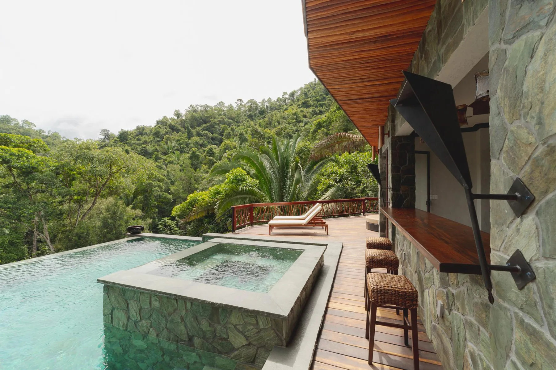 A stone-sided pool and raised water feature sit beside a wooden deck overlooking green hills.