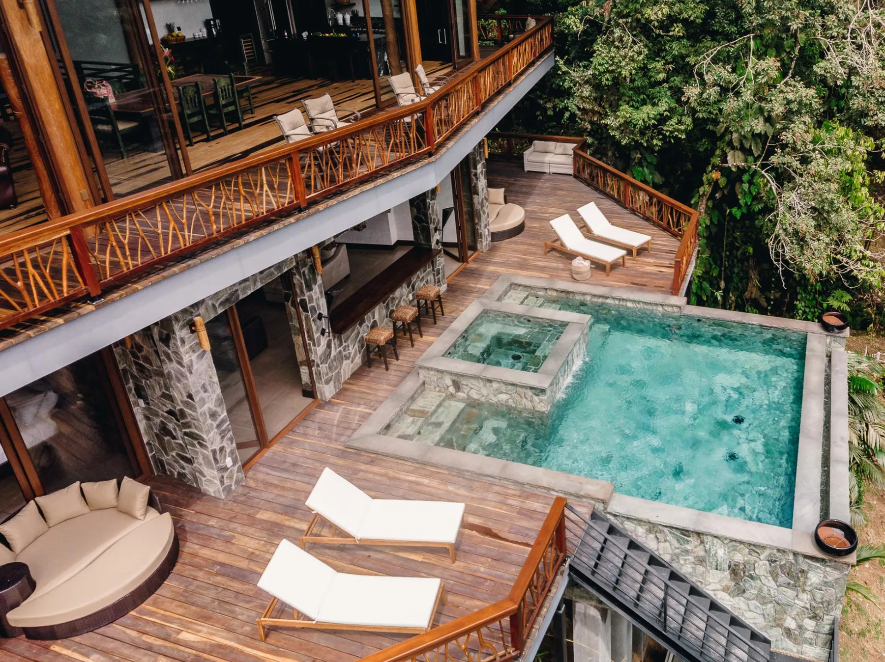An outdoor pool and raised hot tub sit beside a wooden deck with lounge seating.