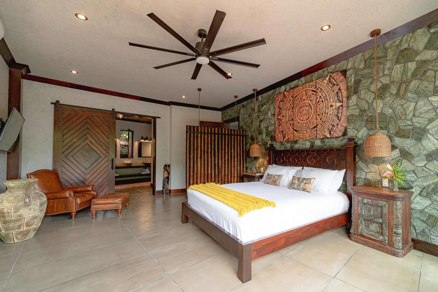 A bedroom with a large bed, patterned wall hanging, and stone accent wall.