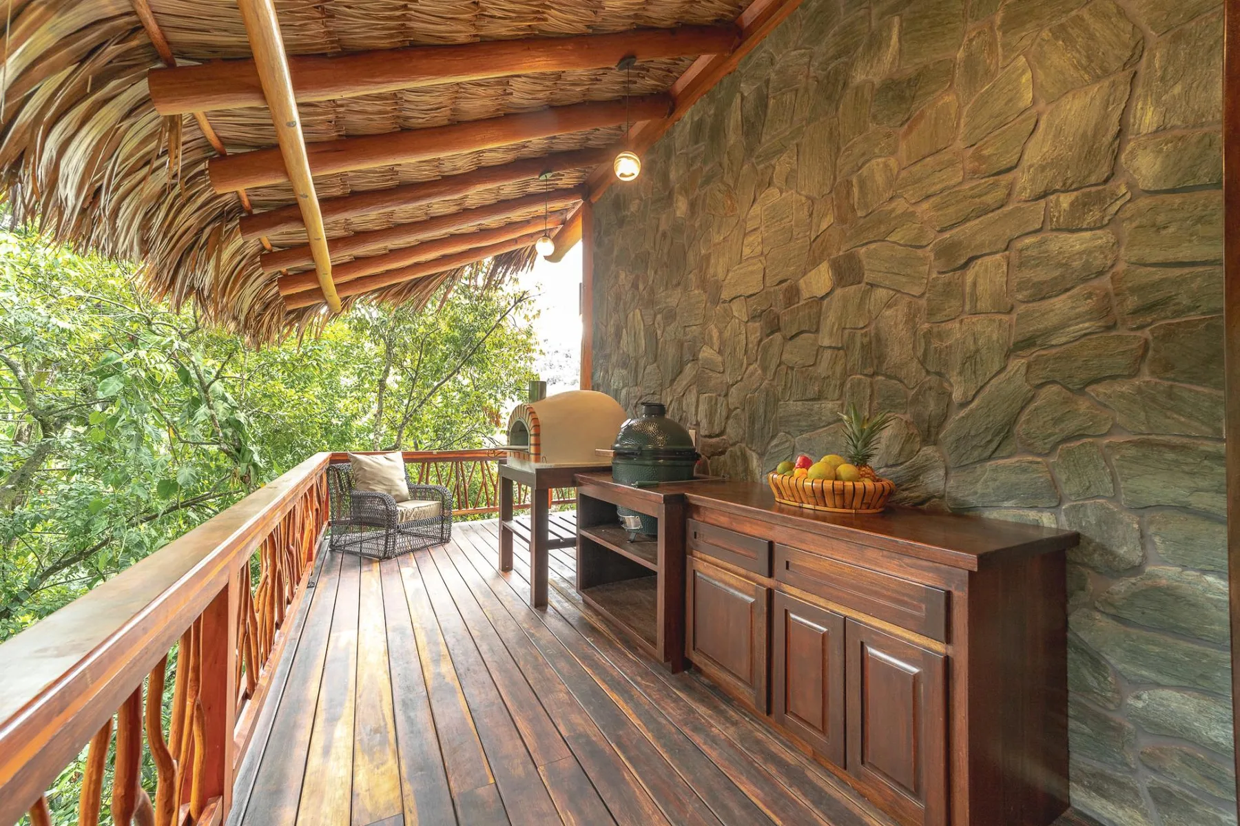 A covered outdoor dining area with a wooden table and fruit bowl beside a stone wall.