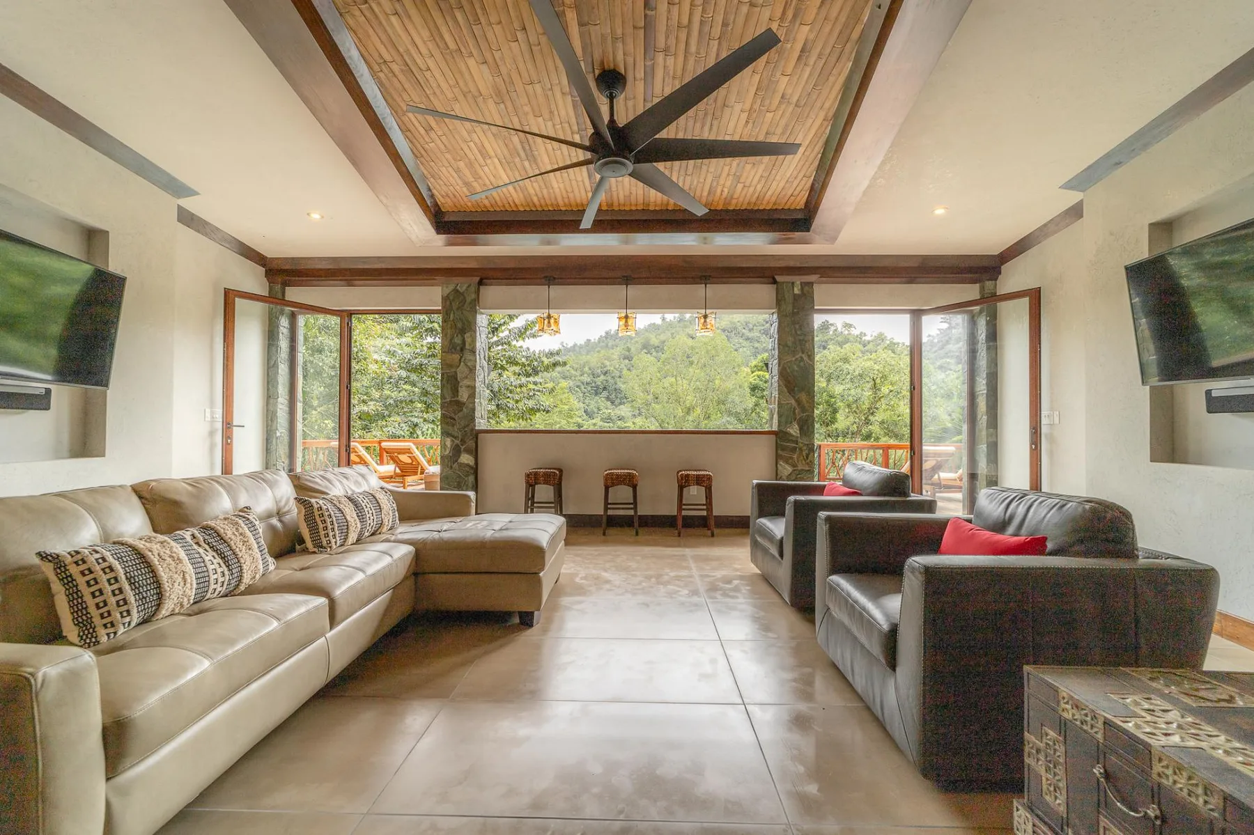 A spacious living room with seating, a ceiling fan, and large windows overlooking greenery.