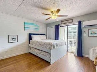 Un dormitorio luminoso con una cama, suelo de madera y cortinas azules junto a una puerta de vidrio.