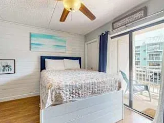 Un dormitorio luminoso tiene una cama junto a grandes puertas de vidrio que dan a un balcón.