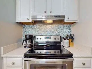 Una zona de cocina con una estufa bajo gabinetes blancos.