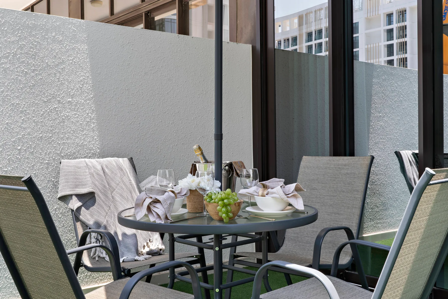 Una zona de comedor al aire libre con la mesa puesta junto a ventanas altas.