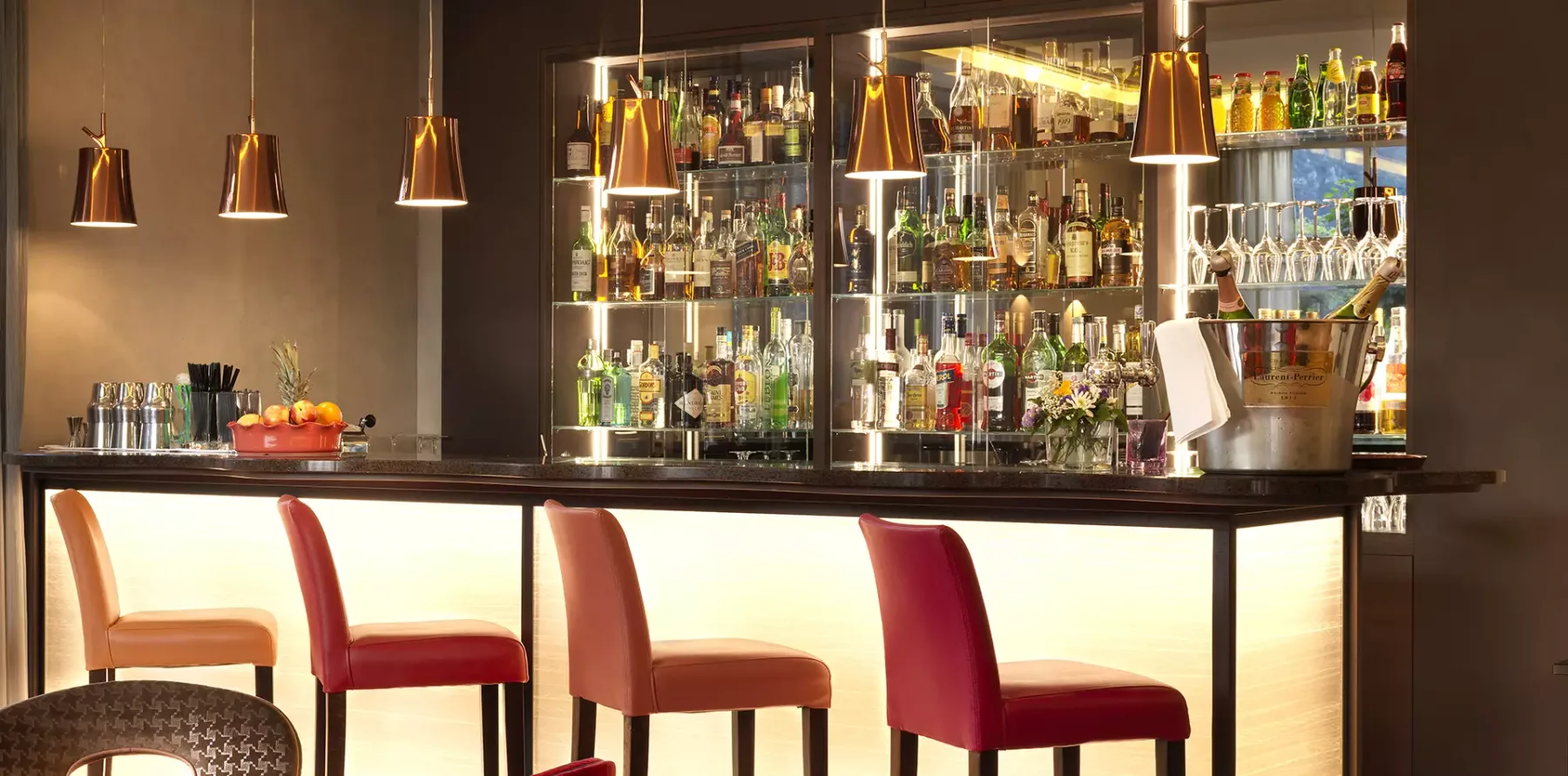 Espacio representativo del hotel: Una barra con botellas de colores exhibidas en estantes iluminados.