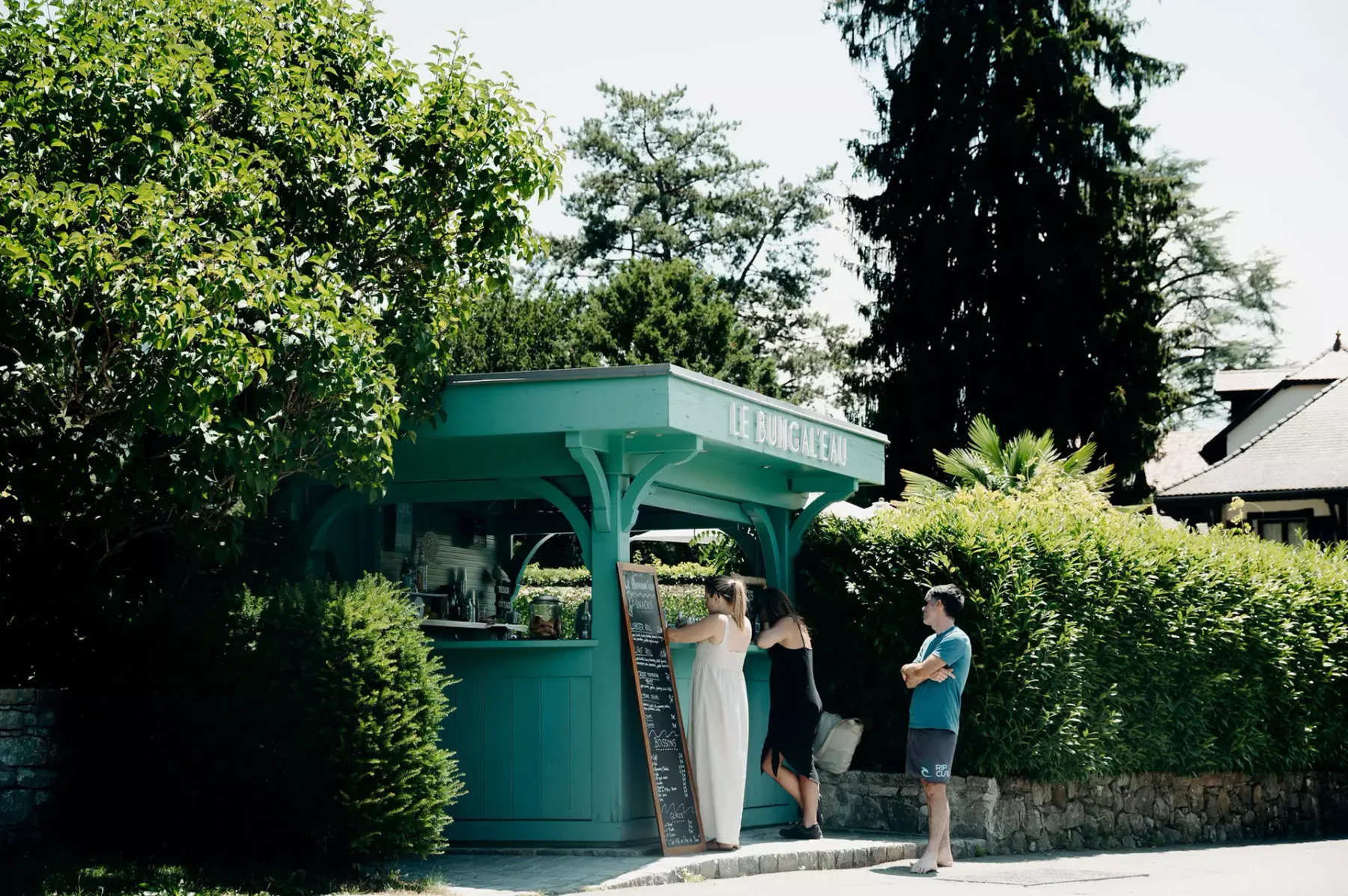 Espacio representativo del hotel: Un quiosco verde azulado al aire libre está entre árboles junto a un sendero pavimentado.