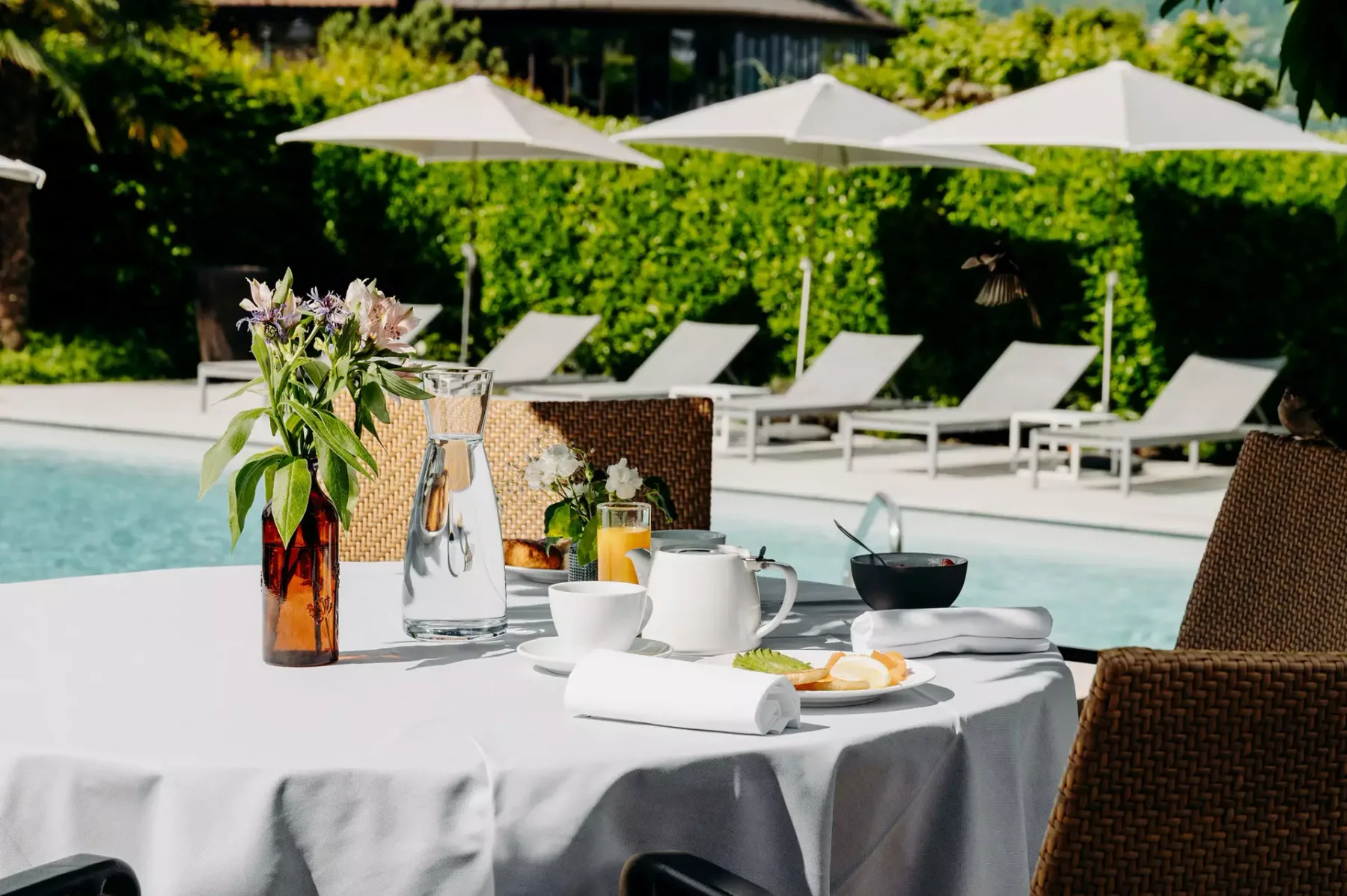 Espacio representativo del hotel: Una mesa junto a la piscina está preparada con bebidas y flores junto al agua.