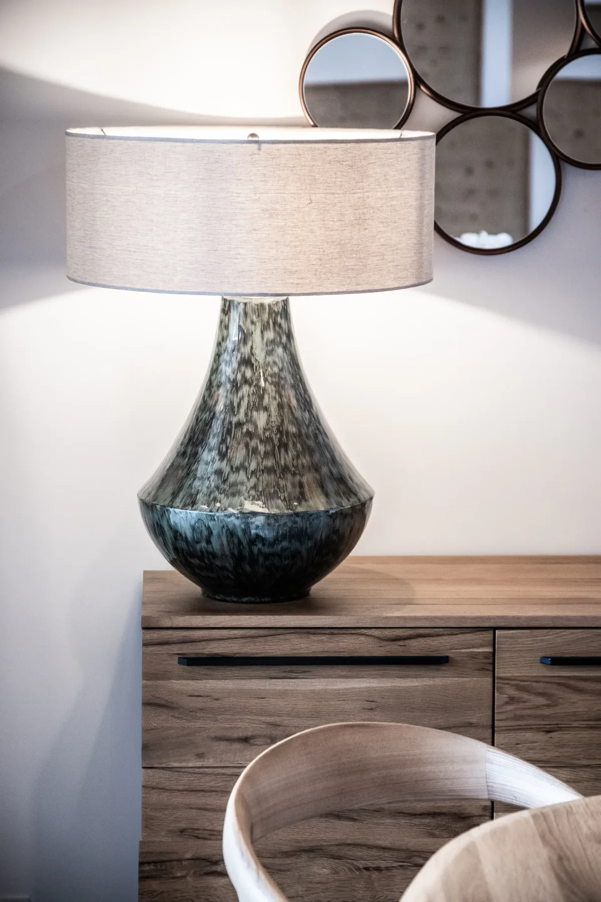 Una lámpara de mesa está sobre una cómoda de madera, debajo de un espejo redondo.