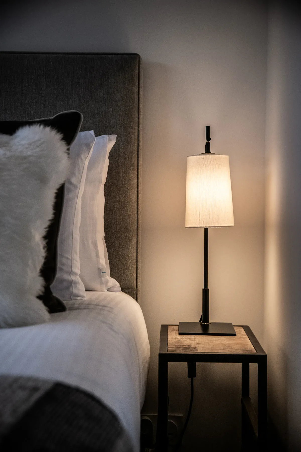 Un dormitorio con una mesita de noche y una lámpara encendida junto a la cama.