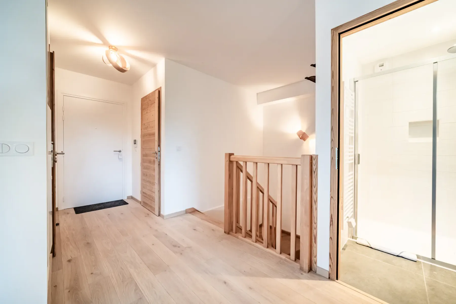 Un pasillo luminoso en la planta superior con una barandilla de madera y la puerta abierta de un baño.