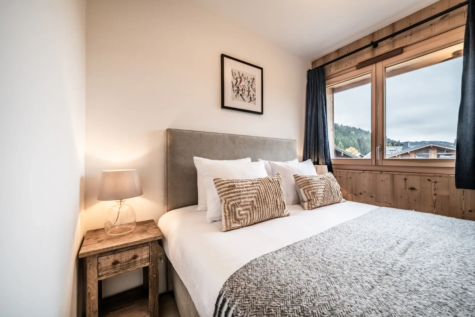 Un dormitorio con una cama bien arreglada junto a una ventana grande.