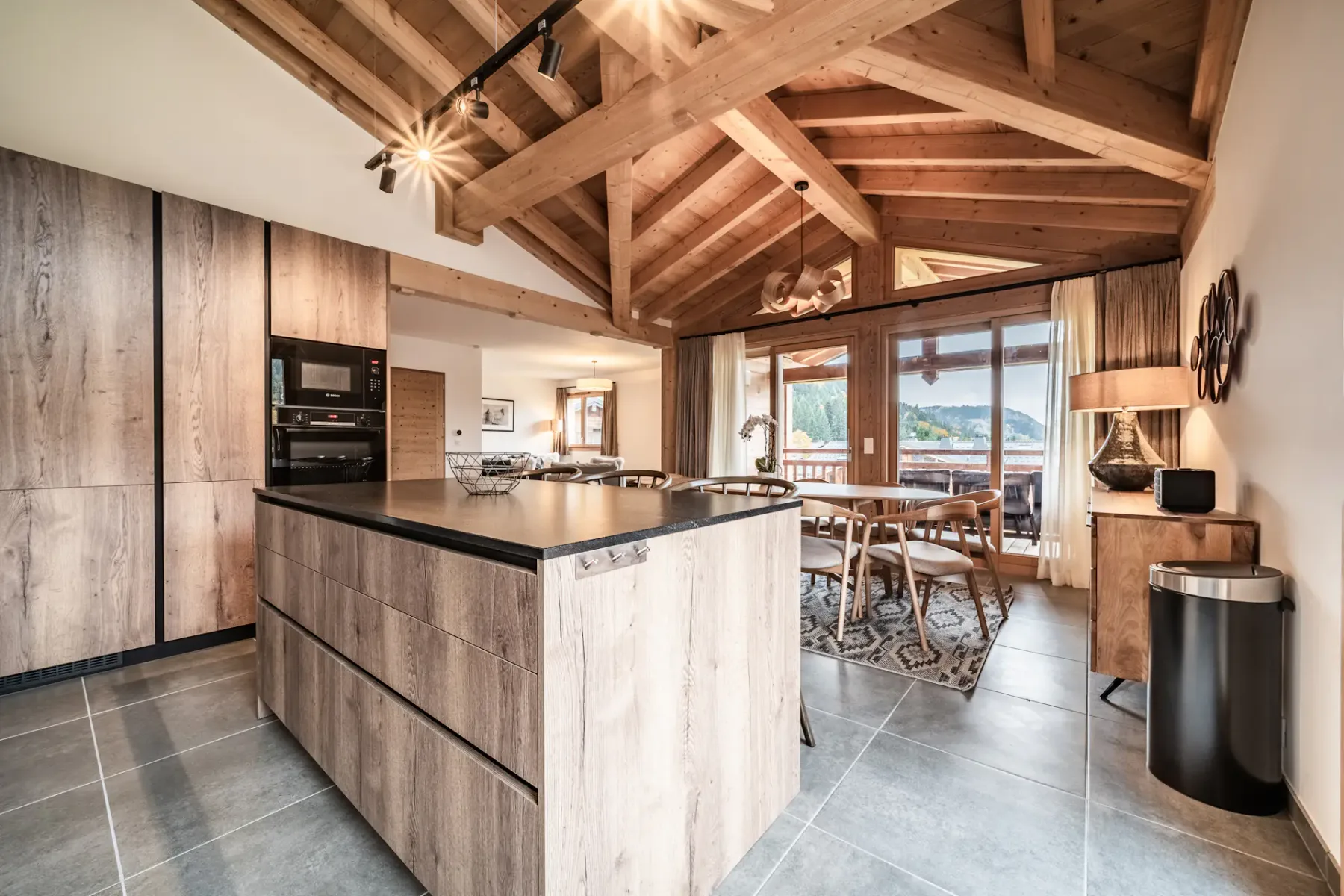 Una cocina se abre a un comedor bajo vigas de madera expuestas.