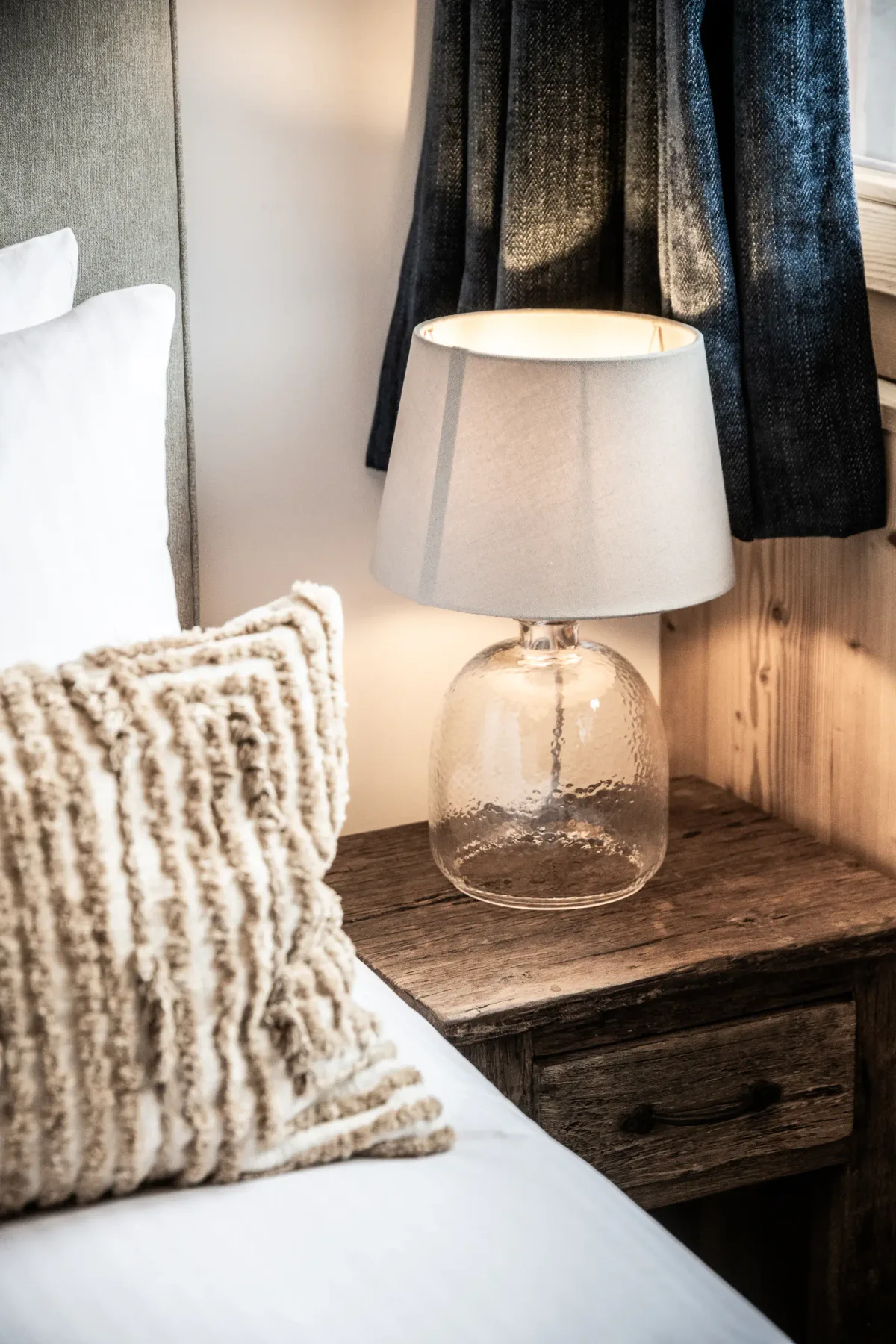Una mesa junto a la cama sostiene una lámpara encendida.