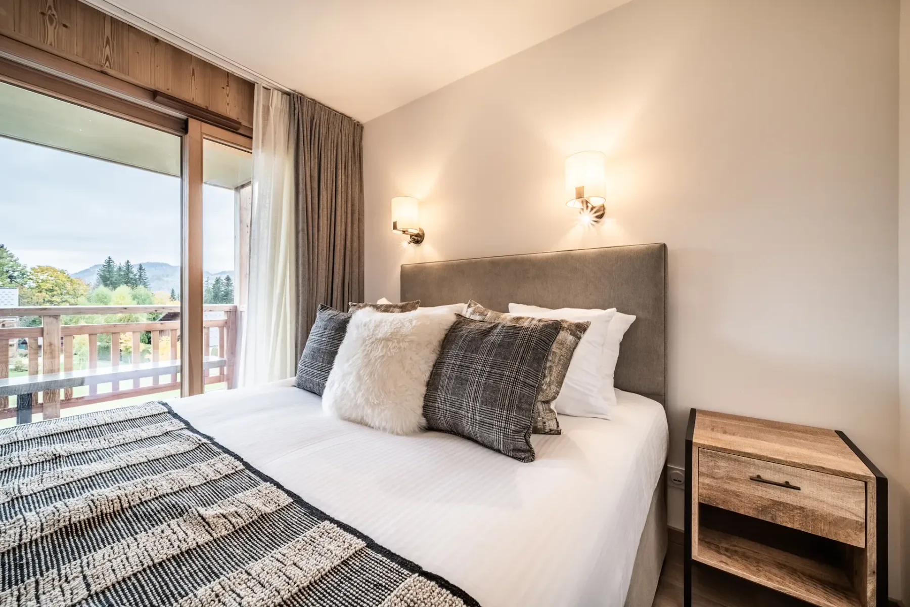 Un dormitorio con una cama bien tendida junto a una gran puerta acristalada que da a un balcón.