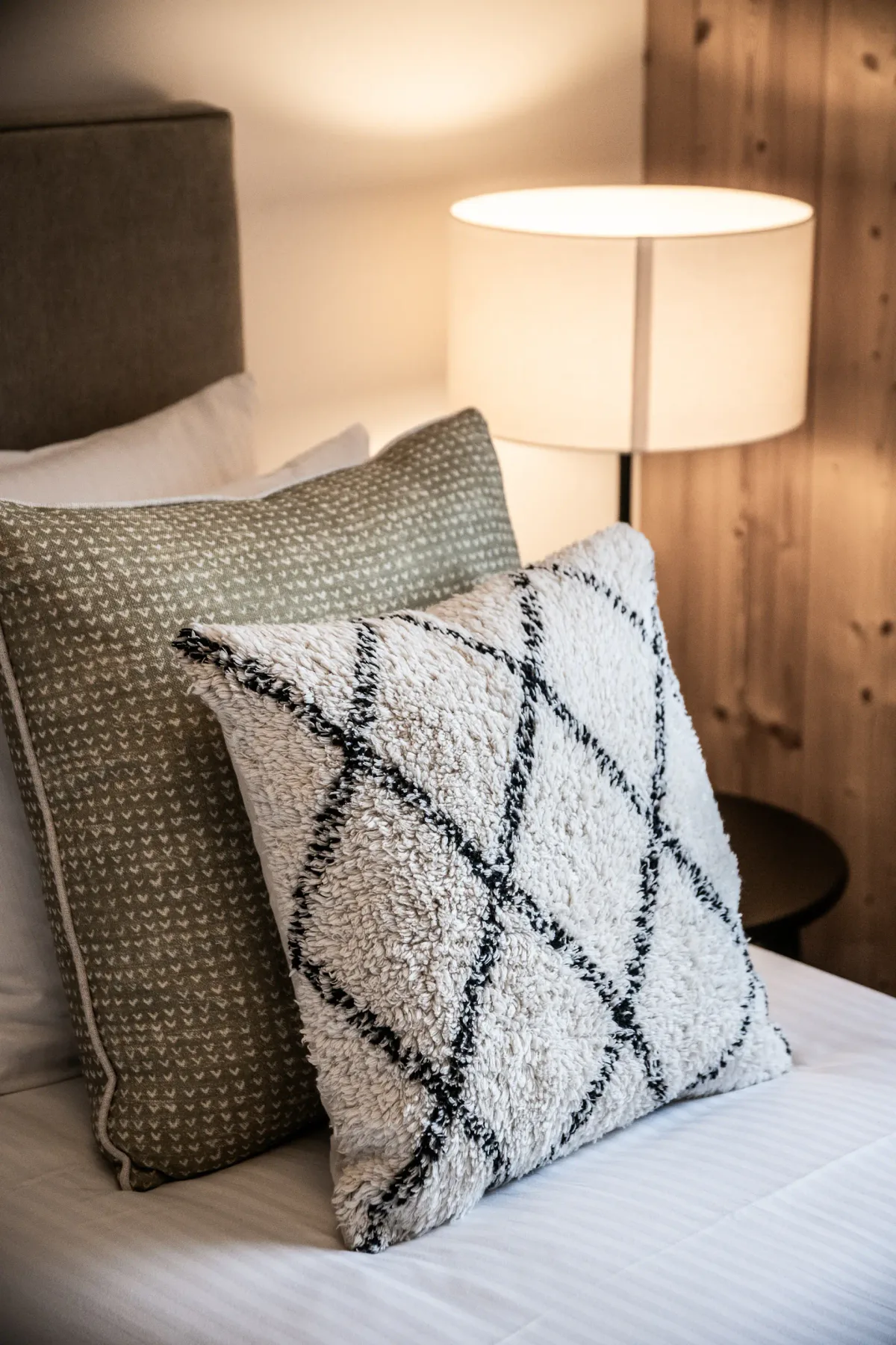 Una cama con almohadas estampadas está junto a una lámpara de mesa encendida.