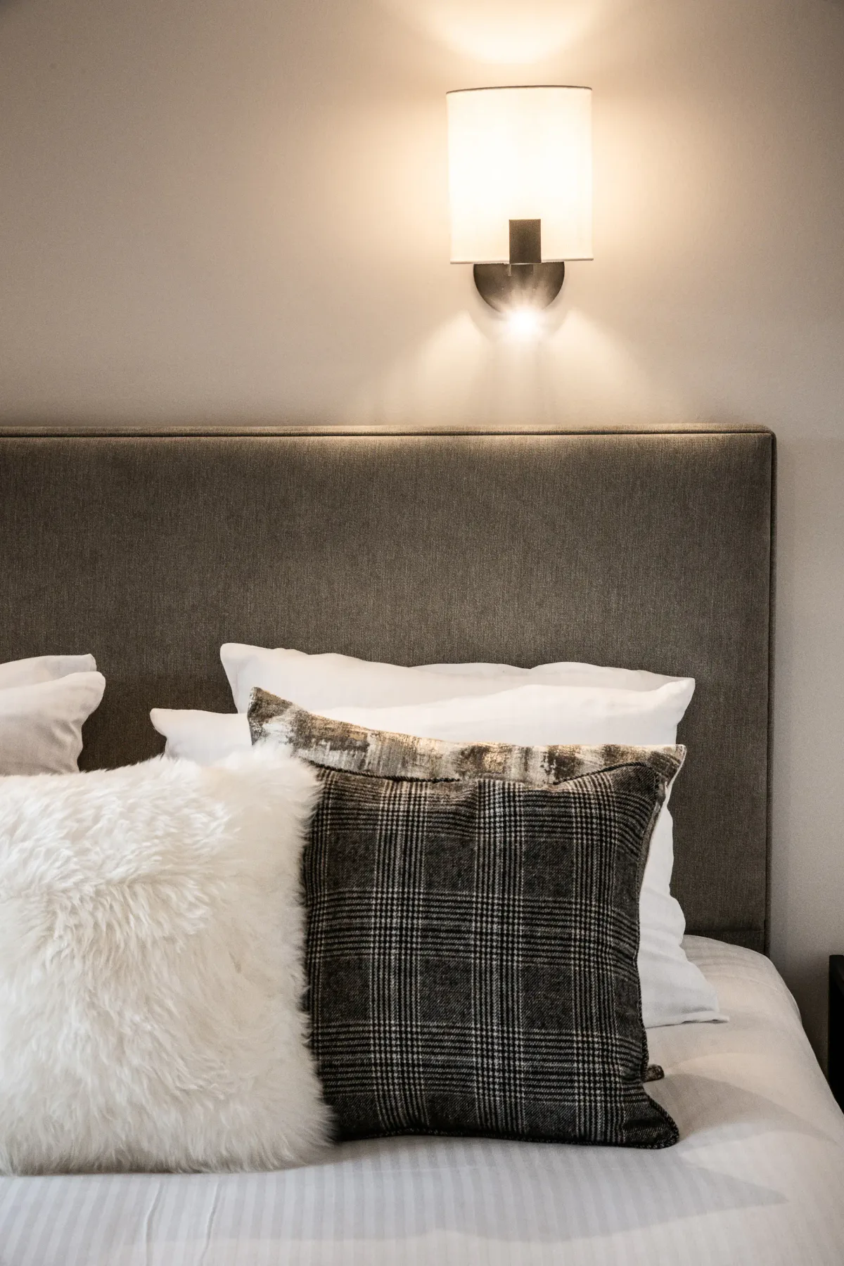 Una cama con varias almohadas está bajo una lámpara de pared encendida.