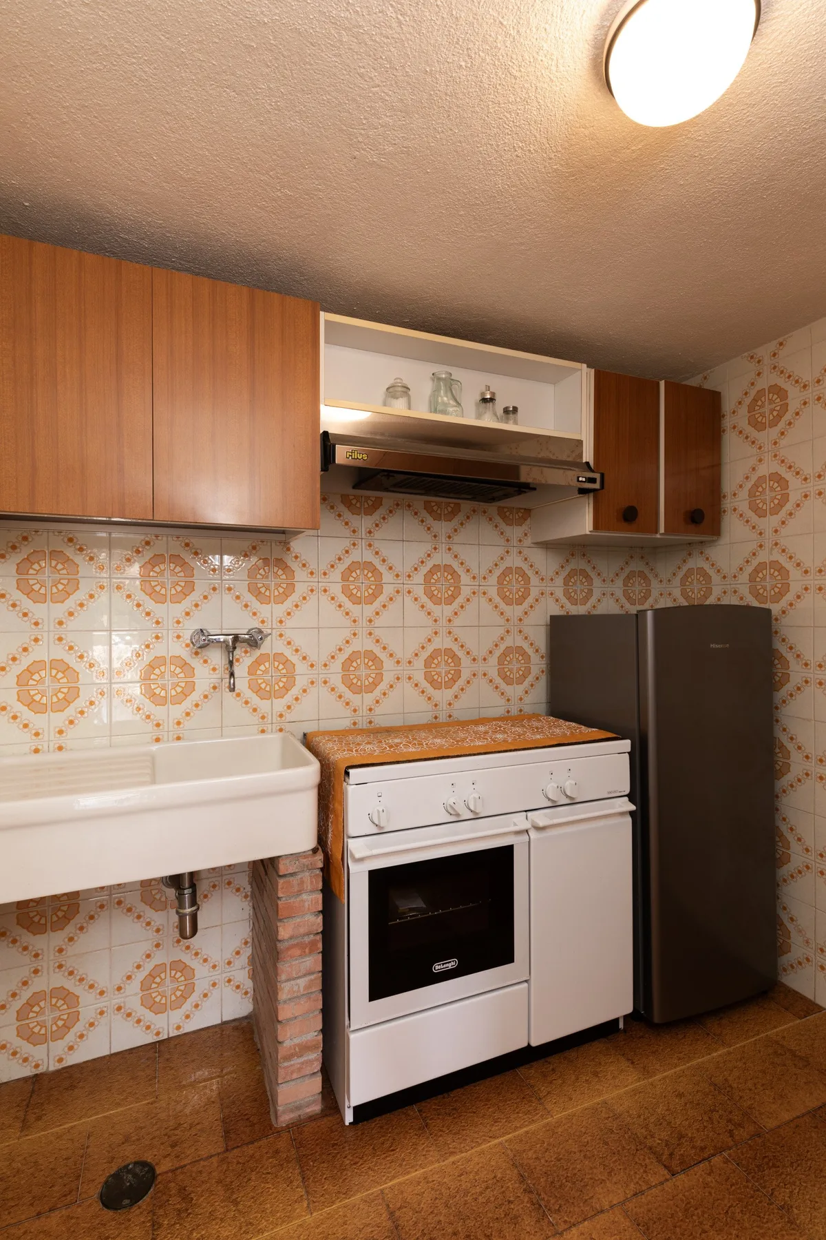 A small kitchen with a sink, stove, refrigerator, and patterned tile walls.
