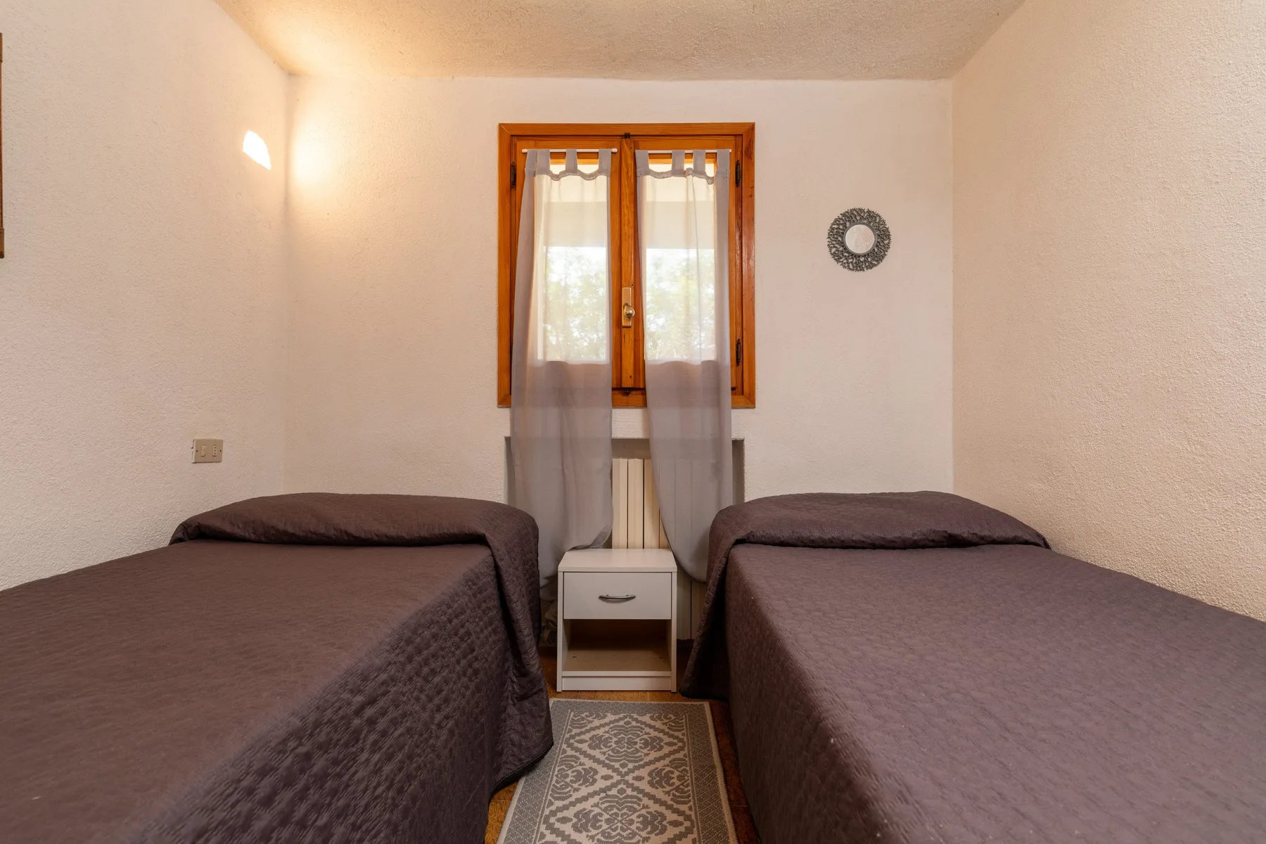 A bedroom with two beds beneath a curtained window.