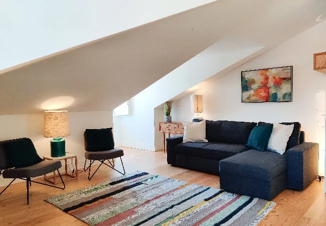 A sloped-ceiling living room with a dark sofa and a striped rug.