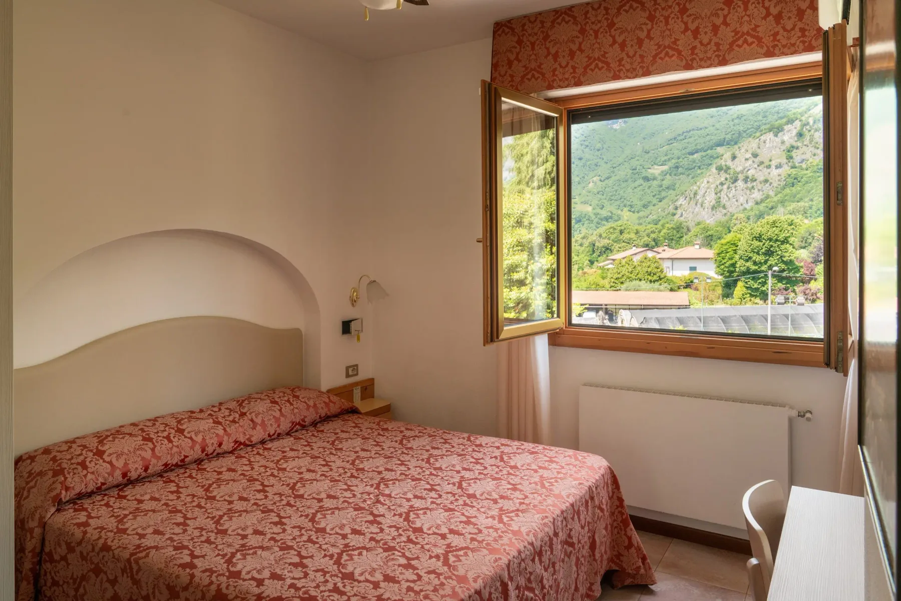 Representative hotel space: A bedroom with a patterned bedspread and an open window overlooking green hills.