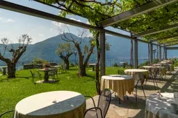 Representative hotel space: Outdoor dining area with tables beneath a leafy pergola, overlooking a garden.