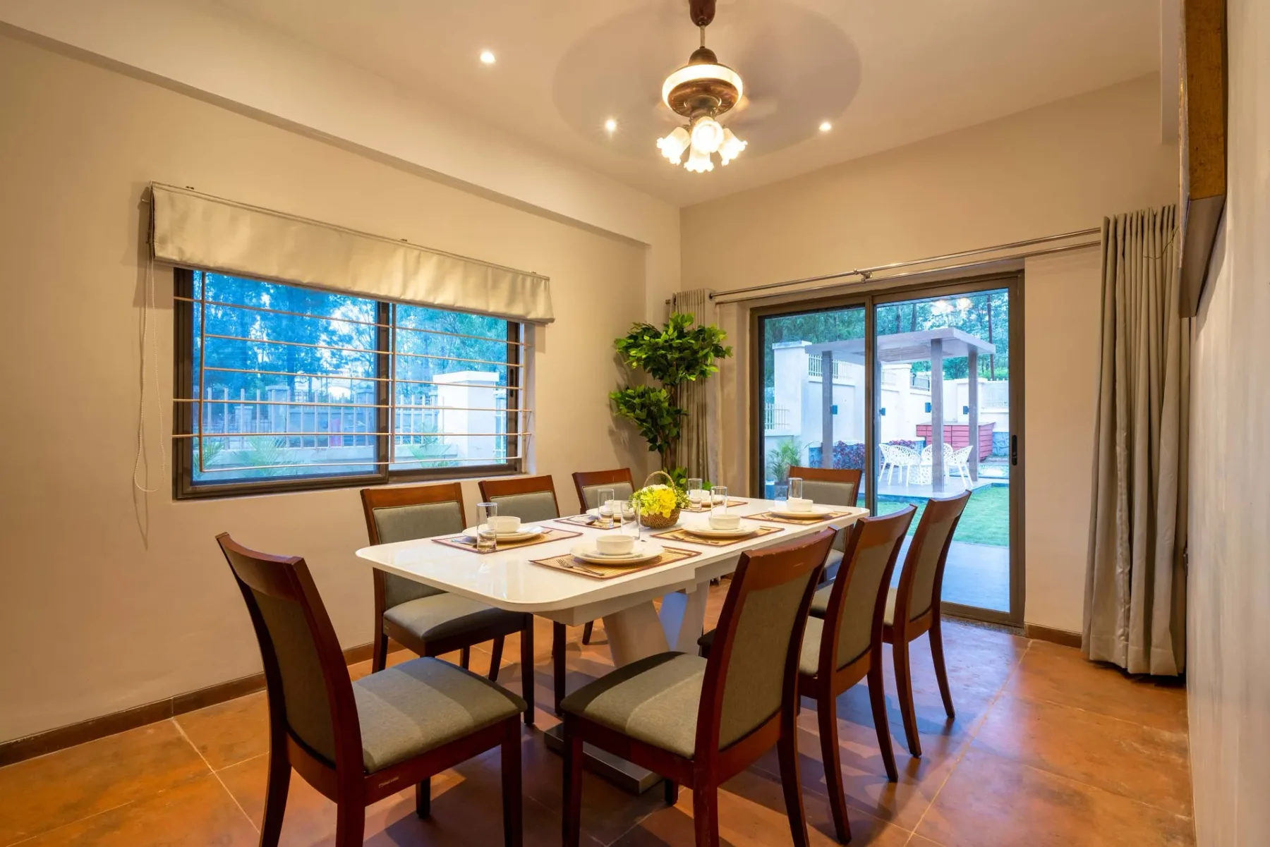 Comedor con la mesa puesta junto a grandes ventanas y una puerta corrediza de vidrio.