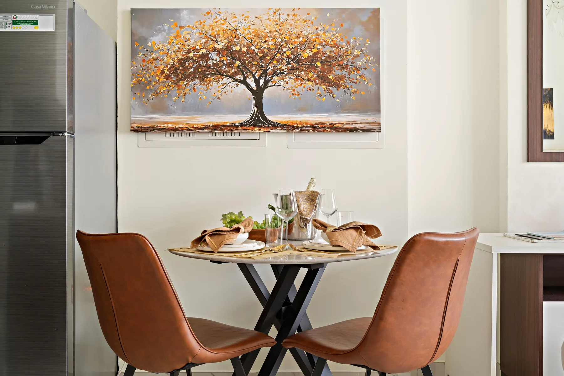 Un comedor con dos asientos alrededor de una mesa bajo un cuadro grande de un árbol.