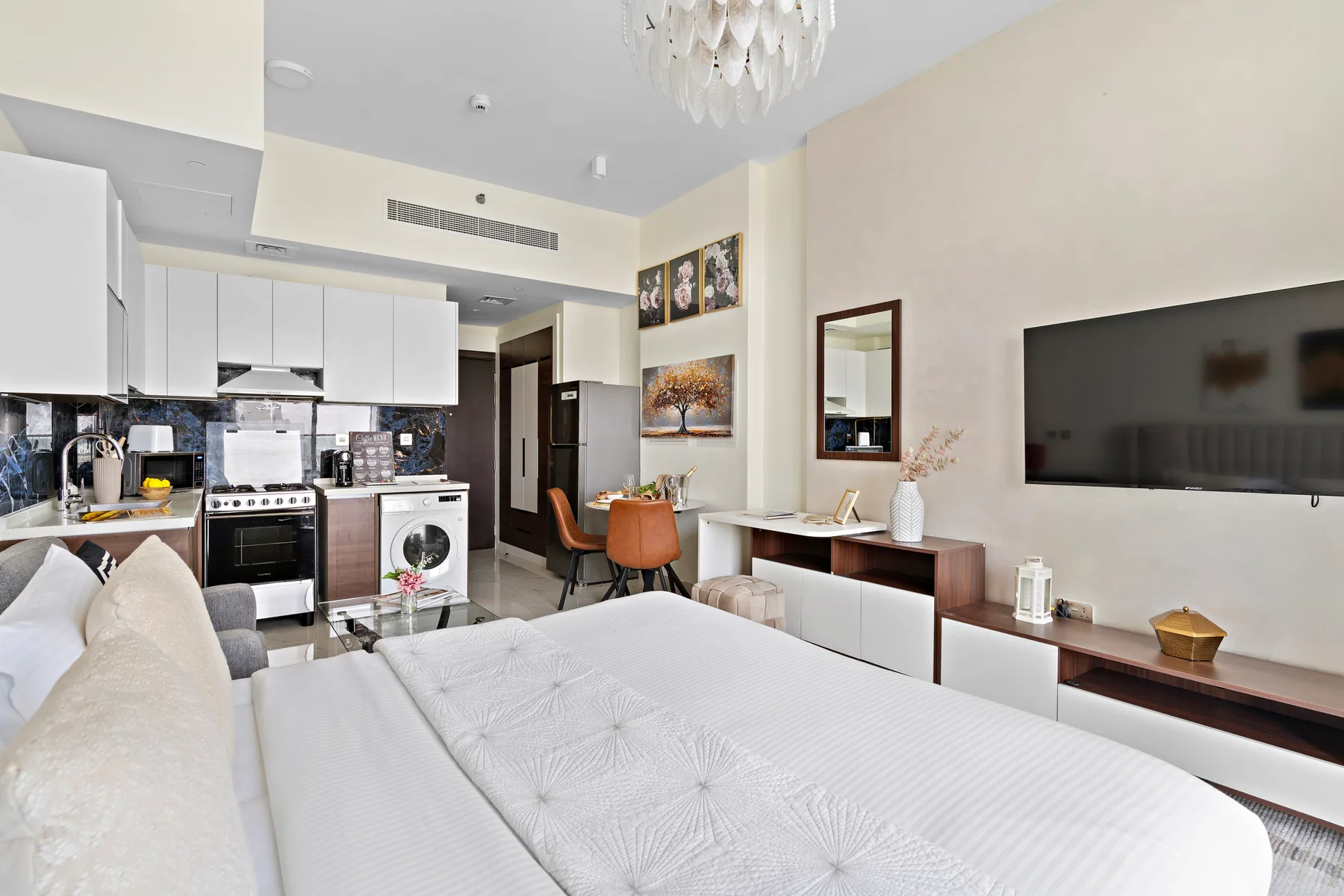 Una luminosa habitación tipo estudio combina una cama, una cocina compacta y un televisor en la pared.