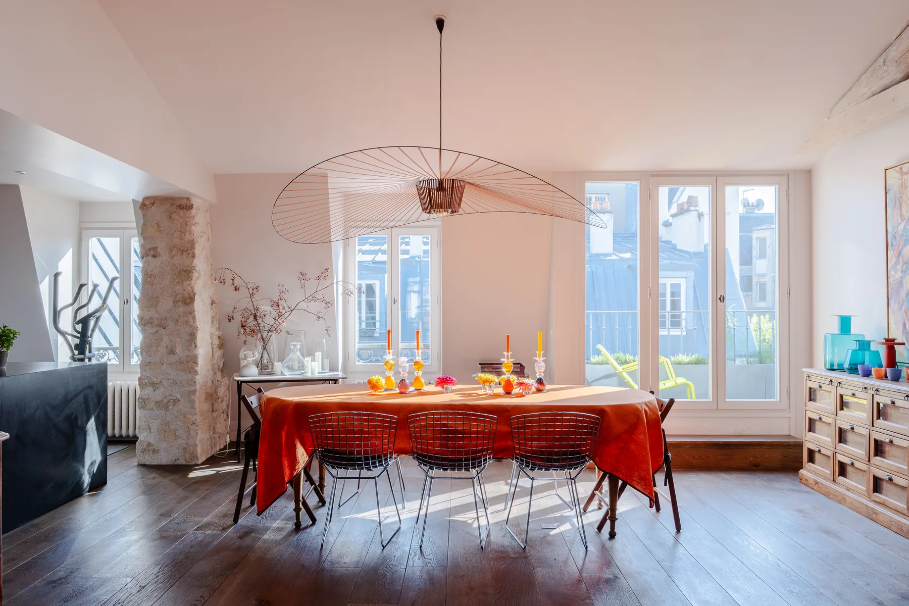 A dining area with a long table covered in a red tablecloth beside tall windows.