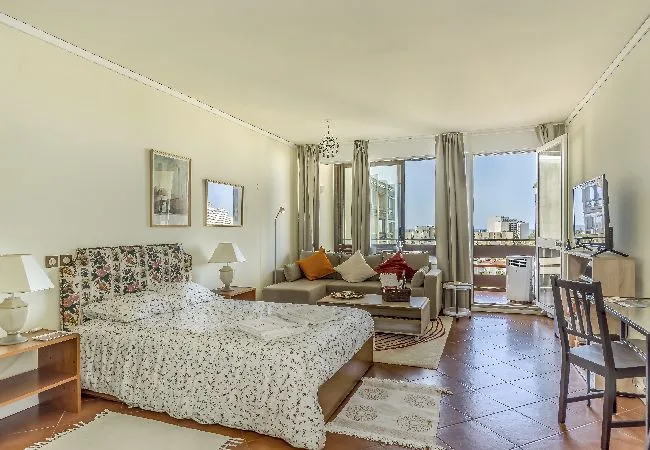 A bright bedroom with a large bed, seating area, and windows opening onto a balcony.