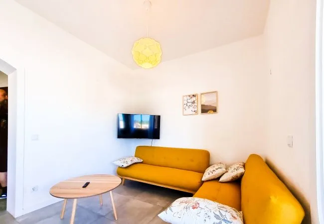 Una sala luminosa con asientos color mostaza, un televisor y una mesa de centro redonda.